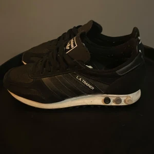  Adidas L.A. Trainer sneakers - Snygga svarta Adidas L.A. Trainer sneakers med klassisk design och snörning. Skorna har en vit sula med justerbara pluggar för optimal komfort och stil. I bra skick bara att mockan bak på en av skorna har en fläck se på sista bilden. Tveka inte att kontakta vid eventuella frågor😀