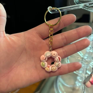 Söt nyckelring med rosa figurer - Nyckelring med en rund dekoration av små rosa figurer med olika ansikten och uttryck. Hängs på en guldfärgad kedja och ring. Perfekt accessoar för att göra dina nycklar extra gulliga.