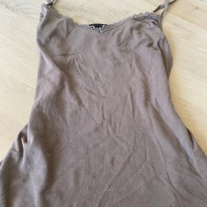 Beige/brun linnetopp med spets från Vero Moda - (Pris går att diskutera) Supersöt beige linnetopp från Vero Moda med tunna axelband och v-ringning dekorerad med spetsdetaljer. Perfekt att styla med jeans eller kjol för en chill look. Mjuk och skön känsla, passar till många outfits.❤️