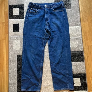 Blå loose fit jeans från H&M - Säljer ett par blå loose fit jeans från H&M med justerbar midja. Klassisk femficksmodell i denim med raka ben och avslappnad passform. Perfekta för en chill och avslappnad stil.