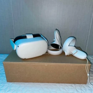Oculus quest 2 - Bilderna visar ett VR-headset med tillhörande handkontroller, Oculus Quest. Produkten är vit och är i mycket bra skick. Perfekt för dig som vill uppleva spel och digitala världar på ett helt nytt sätt! Laddad med möjligheter för gaming och interaktiva upplevelser.