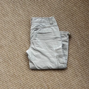 Grå capribyxor från Ann Taylor Loft - Snygga ljusgrå capribyxor från Ann Taylor Loft med justerbara benslut. Storlek 0 (amerikansk). Två fickor fram pch två fickor på varje ben. Byxorna är i bomull och har en avslappnad passform med croppad längd. Perfekta för en chill och casual stil. 