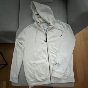 beiga hoodie från Björn Borg i storlek M.  - beiga hoodie från Björn Borg i storlek M. Tröjan har huva med snörning, hel dragkedja framtill och två fickor. Mjuk bomullskänsla och diskret logga på ärmen. 