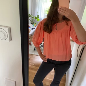 Ljusrosa blus med knyt i halsen - Supersöt ljusrosa blus med trekvartsärmar och knytband vid halsen. Blusen har en lös och luftig passform med fina rynkade detaljer och lätt transparent tyg. Perfekt för en chill och trendig look.