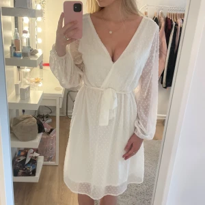 Vit omlottklänning - Superfin vit kort omlottklänning med  diskret prickigt mönster. Klänningen har ett band och en zipledja där bak (sisra bilden) Perfekt nu inför sommaren!