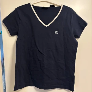Mörkblå t-shirt med v-ringning från FILA - Mörkblå t-shirt från FILA med vit kant runt v-ringningen och liten logga på bröstet. skriv privat om har några frågor 🤍