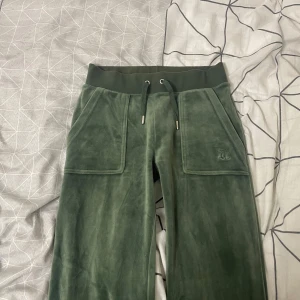 Gröna velourbyxor Juicy Couture XXS - Mörkgröna mjukisbyxor från Juicy Couture i velour med bred resår och snörning i midjan. Byxorna har stora fickor framtill och fickor där bak och broderad JC-logga på ena benet. 