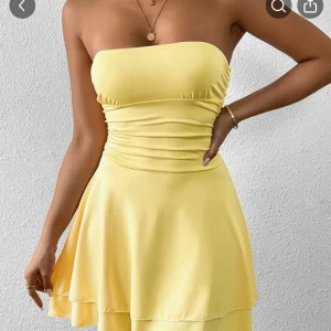 Gul axelbandslös kortklänning - Superfin gul axelbandslös kortklänning med rynkade detaljer i midjan och utsvängd kjol. Klänningen har en mjuk och följsam känsla, perfekt för varma dagar. Enkel men ändå riktigt snygg och lätt att styla med smycken.