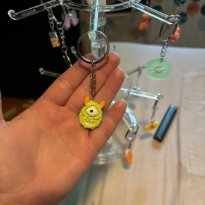 Gult monsterörhänge med öga - Coolt örhänge med en hängande figur av ett gult monster med ett stort öga och orange öron. Smycket har en kedja i silverfärg och är perfekt för dig som gillar unika och lekfulla accessoarer.