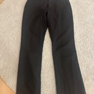 Svarta kostymbyxor från BikBok - Svarta lågmidjade kostymbyxor från BikBok i klassisk rak modell. Byxorna har hällor för bälte, diskreta bakfickor och en stilren look som passar till allt. Perfekta för dig som gillar en clean och enkel stil. 