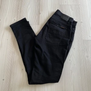 Nudie jeans tight Terry - Svarta jeans från Nudie Jeans med klassisk femficksdesign och svarta sömmar. Jeansen har hög midja och är tillverkade i stretchig bomullsdenim för en tight passform. Perfekta för dig som gillar en stilren och enkel look. Modellen tight Terry, skinny fit. Nästan aldrig använda och ser helt oanvända ut, 10/10 skick!. Storlek 33/34.