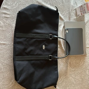 Svart Dolce & Gabbana weekendväska - Stor svart weekendväska från Dolce & Gabbana Beauty med stilren design, dubbla handtag i skinn och silverfärgad kron-detalj framtill. Väskan har dragkedja upptill och är tillverkad i slitstark polyester.