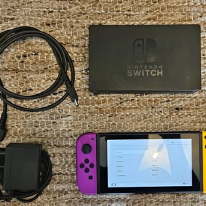 Nintendo switch. - Bilderna visar en Nintendo Switch-konsol med tillbehör, inklusive laddare och dockningsstation. Konsolen har färgglada Joy-Con-kontroller i lila och gult. Perfekt för gaming på språng eller hemma, och passar dig som vill spela både solo och med vänner.