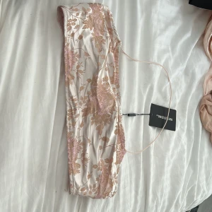 Blommig topp  - Supersnygg topp från PrettyLittleThing i ljusbeige med broderade blommor i rosa och guld. Tunn axelrem och elegant, croppad passform. Köpt för 400