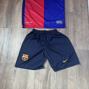 FC Barcelona Lamine Yamal matchtröja Nike - FC Barcelona matchtröja med Lamine Yamal 19-tryck, tillverkad i Dri-FIT-material från Nike. Klassisk design i rött och blått med gula detaljer, klubbmärke och La Liga-patch på ärmen. Kortärmad och randig, perfekt för dig som älskar Barca.