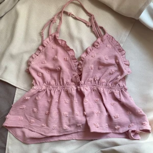 Rosa blommig linnetopp - Supersöt rosa linnetopp från SHEIN med små broderade blommor och volangdetaljer längs v-ringningen. Toppen har smala axelband som korsas i ryggen och en lätt rynkad midja för en luftig känsla. Perfekt för varma dagar när du vill känna dig extra gullig.