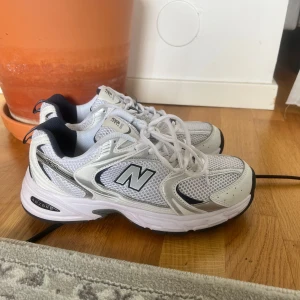 Vita New Balance 530 sneakers - Använda 3 gånger Säljer ett par klassiska New Balance 530 sneakers i vitt med silverdetaljer och svart sula. Skorna har meshpaneler för extra andningsförmåga, snörning och en chunky retro vibe. Perfekta för dig som gillar sportig och trendig stil.