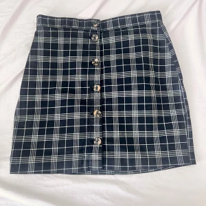 Svartvit rutig kortkjol med knappar - Snygg svartvit rutig kortkjol med raka linjer och knappar hela vägen framtill. Kjolen har en klassisk, lite preppy vibe och passar perfekt till en stickad tröja eller t-shirt. Tidlös design som är lätt att matcha.