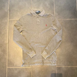 Grå pikétröja från Ralph Lauren - Säljer nu en snygg grå långärmad pikétröja från Polo Ralph Lauren.Uppgradera din garderob med denna klassiska och bekväma långärmade polotröja från Polo Ralph Lauren. Tröjan är tillverkad i ett mjukt och skönt material och har en tidlös design som passar perfekt för både vardag och mer uppklädda.                                                           Storlek: S  |  Skick: 9/10 (Inga defekter)           Om du har några funderingar eller intresse kontakta mig.