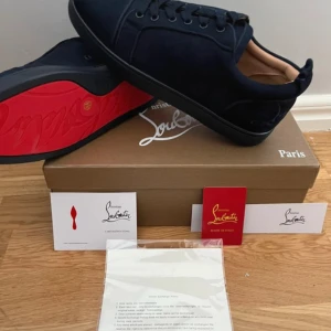 Mörkblå sneakers från Christian Louboutin - Snygga mörkblå sneakers från Christian Louboutin i mocka med klassisk röd sula och broderad logga på hälen. Skorna har rund tå, snörning och en stilren design som sticker ut med den ikoniska röda undersidan. Säljer dom då dom är 42 och jag har 44-45