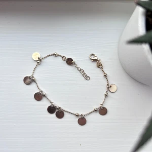 Guldigt armband från Bianca Ingrosso - Ett tunt och stilrent armband i guldfärg med små runda myntberlocker längs hela kedjan. Armbandet har en fin kulkedja och justerbar längd med karbinlås. Perfekt accessoar för att ge din look lite extra shine. Från en av Bianca Ingrossos kollektioner med guldfynd.