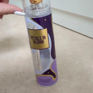 Body Mist - Fräsch body mist med blommig doft från Petals in Bloom. Flaskan är genomskinlig med lila, vitt och guldigt etikett, samt guldfärgad spraydel och genomskinligt lock. Rymmer 235 ml och har en modern, stilren design som passar perfekt i väskan. (Bara sprejat några enstaka gånger för att känna lukten)☺️