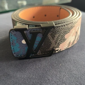 Louis Vuitton rutigt svart bälte - Snyggt bälte från Louis Vuitton med klassiskt rutigt mönster i svart och grått. Bältet har en stor LV-logga i svart metall som spänne och är gjort i skinn med en lyxig känsla. Perfekt accessoar för att lyfta din outfit.