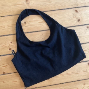 Svart ribbad linnetopp från Shein - Säljer en svart ribbad linnetopp med halterneck och breda axelband. Toppen är croppad och har en tight passform som framhäver axlarna. Storlek M. I fint skick.