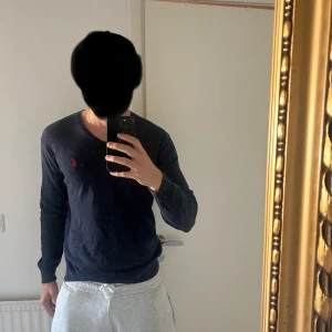 Marinblå v-ringad tröja Polo Ralph Lauren - Snygg marinblå v-ringad tröja från Polo Ralph Lauren med klassisk röd broderad logga på bröstet. Långärmad modell i mjuk bomull, perfekt för lager-på-lager och storleken är S. Skick 9,2/10 (använd ett fåtal gånger). Jag väljer att sälja den pga av att jag behövde fräscha upp garderoben. Om du har frågor tveka inte på att höra av dig. Mvh
