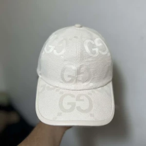 Vit keps från Gucci med GG-mönster - Exklusiv vit keps från Gucci med ikoniskt GG-mönster ton-i-ton över hela kepsen. Kepsen har böjd skärm och justerbar rem baktill. Tillverkad i bomullsmix med snygg struktur och diskret logotyp på insidan. Perfekt för dig som vill sticka ut med stil och folket☀️🫵🏻