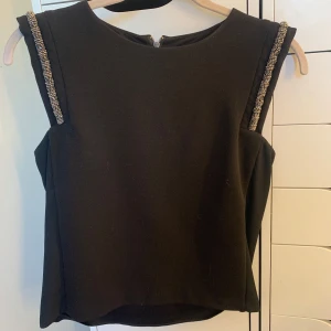 Svart ärmlös topp med pärldetaljer Mango - Snygg svart ärmlös topp från Mango med raka axlar och pärlbroderade detaljer längs axelsömmarna. Toppen har rund halsringning och dragkedja i ryggen. Perfekt för dig som vill ha något stilrent men ändå med lite extra bling. Jätte fint skick🥰🥰