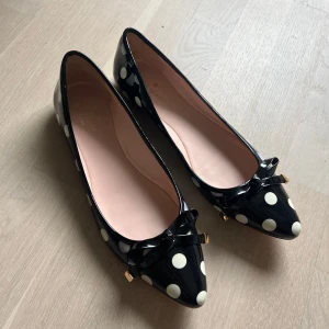 Svartvita Polka Dot Ballerinaskor - Snygga svarta ballerinas från Kate Spade med vita prickar, lackad finish och spetsig tå. Dekorerade med en jättesöt rosett framtill och små gulddetaljer! Stl 41 men passar mer en 40 eller liten 41a