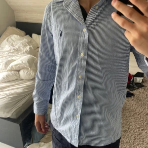 Blårandig skjorta från Polo Ralph Lauren - Riktigt snygg Skjorta, sparsamt använd endast ental gånger. Är själv 170cm, väger 60kg. Passar mig perfekt! 