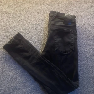 Svarta Replay anbass jeans slim fit - Snygga svarta jeans från Replay med klassisk femficksdesign och diskret logga på bakfickan. Jeansen har en slim passform och är tillverkade i mjuk bomullsblandning med lite stretch för extra komfort.