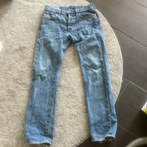 Levi's 501 blå jeans W29 L32 - Klassiska Levi's 501 jeans i ljusblå denim med raka ben och normal passform. Byxorna har fem fickor, knappgylf och den ikoniska läderpatchen bak i midjan. Perfekta för en avslappnad och tidlös stil. Org pris:1300