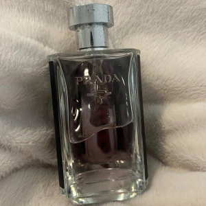 Prada L'Homme Eau de Toilette 100ml - Exklusiv herrparfym från Prada, L'Homme, i en stilren 100ml flaska. Flaskan är transparent med silverdetaljer och har en svart texturerad baksida. Doften är modern och elegant, perfekt för dig som gillar lyxiga och fräscha parfymer.