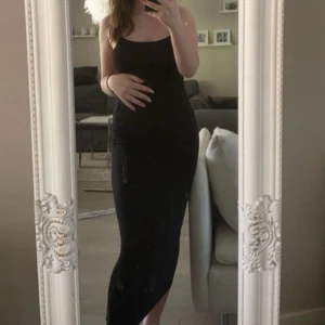 Svart långklänning med smala axelband - En stilren svart långklänning med smala axelband och figurnära passform. Klänningen har en enkel och tidlös design som framhäver siluetten. Perfekt för dig som gillar minimalistisk stil och vill ha något som känns både bekvämt och snyggt.