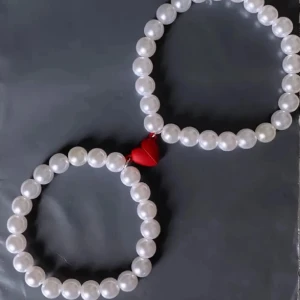 Pärlarmband med rött magnet hjärta - Två elastiska armband med vita pärlor och en söt röd hjärtformad magnet hjärta som binder ihop dem. Perfekt accessoar för att ge din stil en gullig och lekfull touch. Extra gåva på köpet.🛍️