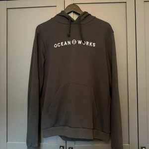 Svart hoodie från Ocean Works - Svart hoodie från Ocean Works med vit logga på bröstet och en liten symbol på huvan. 