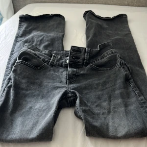 Svarta jeans från Lindex, strl 32 - Utsvängda, low. Snygga svarta jeans från Lindex i storlek 32. Klassisk femficksmodell med knäppning fram och raka ben. Jeansen har en mörk tvätt och är tillverkade i mjukt denimtyg som sitter skönt hela dagen.
