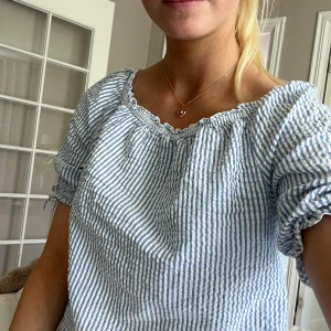 Randig blus med puffärm och knyt - Supersöt blus med ljusblå och vita ränder, puffiga korta ärmar med knyt och rynkad resår vid halsringningen. Luftig och lätt i bomull, perfekt för varma dagar. Sitter lite loose och har en avslappnad vibe.