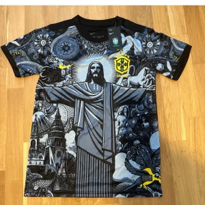 Nike Brasil special edition fotbollströja - Unik Brasilien fotbollströja från Nike med konstnärligt tryck av Kristusstatyn och brasilianska motiv i svart, blått och gult. Kortärmad modell med svart rygg och detaljerat mönster framtill. Perfekt för dig som vill sticka ut på läktaren eller gatan.