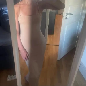 Beige långklänning med smala axelband - Supersnygg beige långklänning med smala axelband och öppen rygg. Klänningen är figurnära och har en enkel, stilren design som passar perfekt för sommaren. Materialet känns mjukt och följsamt mot kroppen. Perfekt för dig som gillar minimalistisk och trendig stil. Har en liten vit fläck som syns i vissa ljus, men inte så märkvärdig