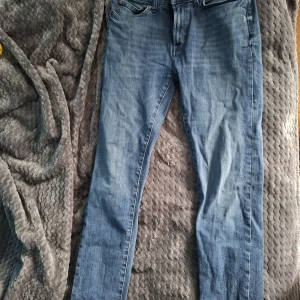 Blå slim fit jeans från Dressmann - Snygga blå jeans från Dressmann i modellen slim fit. Klassisk femficksdesign, normalhög midja och raka ben. Jeansen är tillverkade i bomull och har en ljusblå tvätt som ger en avslappnad vibe. Perfekta för dig som gillar en smalare passform.