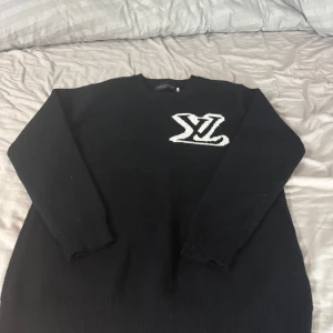 Svart stickad tröja Louis Vuitton - Svart stickad tröja från Louis Vuitton med vit LV-logga på både fram- och baksidan. Den är använd endast 1 gång. Det är storlek XL men passar både L och M