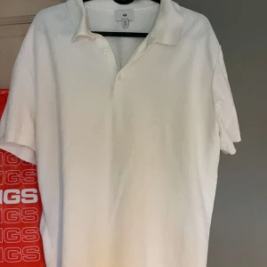 Vit pikétröja från H&M i bomull - Klassisk vit pikétröja från H&M i mjuk bomull. Tröjan har korta ärmar, krage och knäppning med två knappar framtill. Regular fit som passar till många olika stilar. Perfekt för dig som gillar en clean och enkel look.