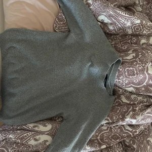 Grå stickad tröja från Vero Moda - Mysig grå stickad tröja från Vero Moda i storlek XS. Tröjan har en klassisk rund halsringning, ribbade muddar och lång ärm. Perfekt för lager-på-lager och enkel att matcha med jeans eller kjol.
