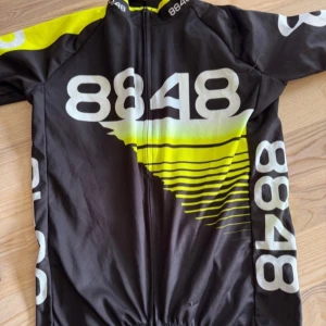 8848 cykeltröja i svart och neon - Snygg cykeltröja från 8848 i svart och neon-gult med stora logotyper och coolt grafiskt mönster. Tröjan har dragkedja framtill, korta ärmar och praktiska fickor bak. Perfekt för dig som vill sticka ut på cykelturen!