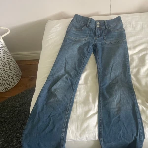 Blå bootcut jeans med låg midja - Säljer ett par snygga blå jeans med bootcut-modell och låg midja från Nelly. Jeansen har dubbla knappar framtill, klassiska fickor både fram och bak samt coola detaljer på bakfickorna. 