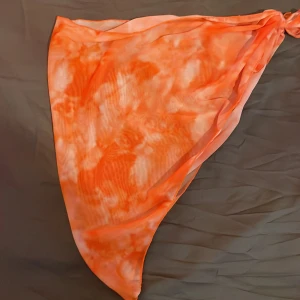 Orange strankjol med knyt i midjan - Snygg orange bikiniunderdel med knyt i sidan och coolt mönster. Tillverkad i stretchig polyester och spandex som sitter skönt på kroppen. Perfekt för stranden eller poolen när du vill sticka ut med färg och stil.